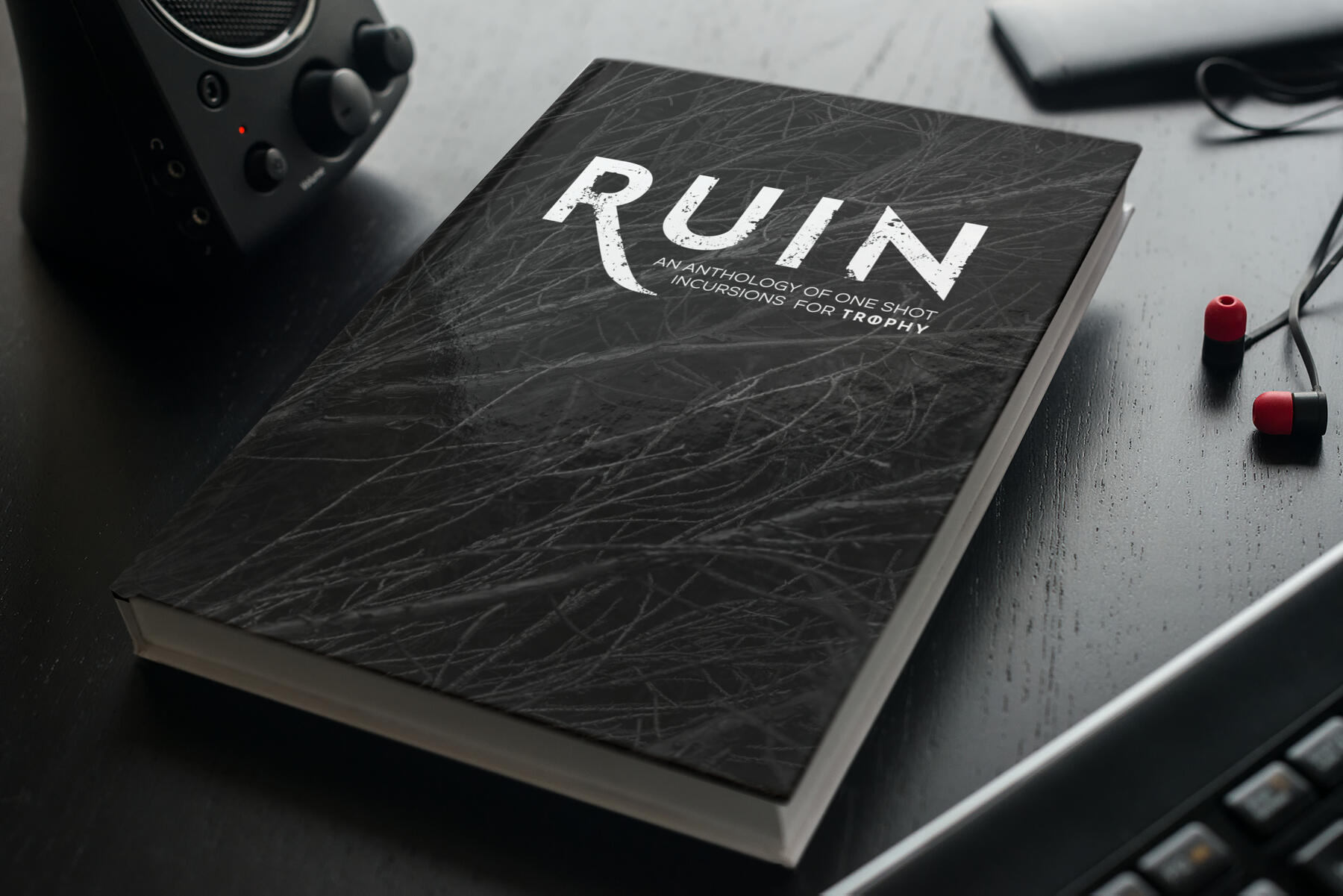 Mock Up of Ruin A hardcover book on a desk surrounded by gadgets (for playing Trophy online, probably!)